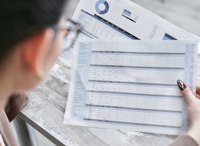 A businesswoman reviewing financial spreadsheets with charts and graphs in an office setting.